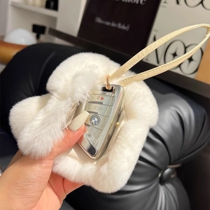 Close-up of white rabbit fur car key cover with leather strap held in hand
