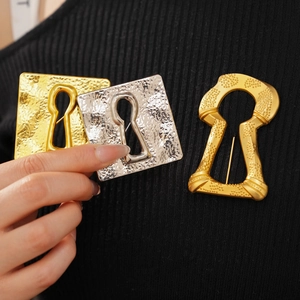 Detailed view of vintage gold and silver square keyhole brooches on a black knit garment