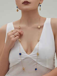 Close-up of gold heart necklace and blue gemstone earrings worn by a model in white dress