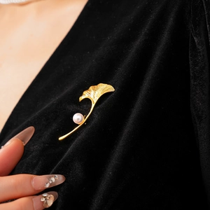 Detailed view of gold plated ginkgo leaf brooch with pearl on black velvet fabric