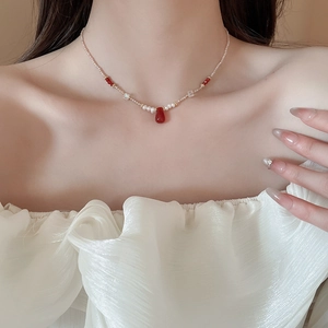 Detail of 18k gold-plated pearl necklace featuring a red teardrop pendant and beads