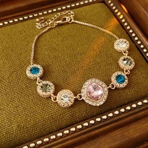 Detail of rose gold bracelet with colorful gemstones on a green velvet cushion