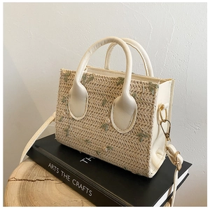 Detail of straw woven handbag featuring green floral embroidery and beige leather straps