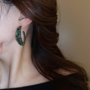 Macro shot of C-shaped earrings with dark green and grey crystals on gunmetal finish
