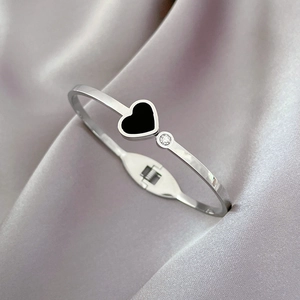 Close-up of silver steel cuff bracelet featuring a black heart charm and small crystal