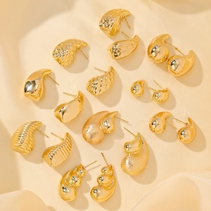 Set of seven gold earrings with shell and teardrop designs on yellow silk background