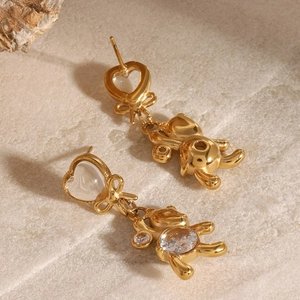 Détail de boucles d'oreilles cœur dorées avec nœud et pendentifs ours en zircon sur pierre