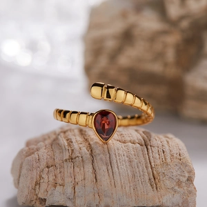 Macro detail of the golden textured open ring featuring a red pear-cut gemstone