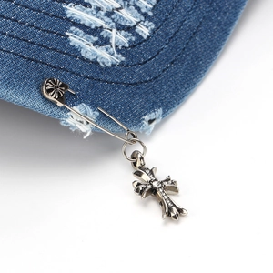 Detail of silver safety pin and cross pendant with zircon on blue distressed denim cap