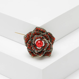 Vintage bronze rose brooch with red beads and central pearl on elegant white background