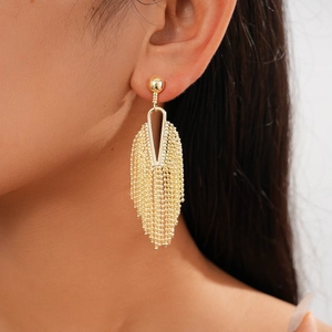 Detail shot of golden geometric hollow tassel earrings worn on a model with long metal chains