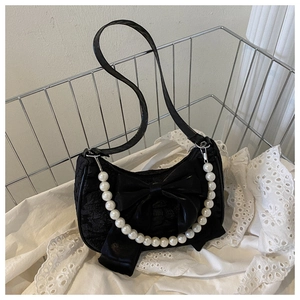 Close-up of black textured shoulder bag with bow and pearl chain in vintage setting