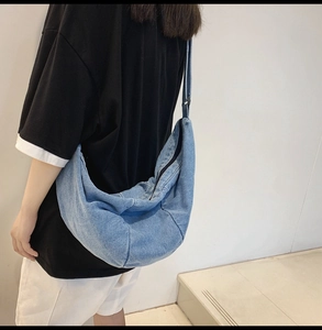 Detail of light blue denim crescent crossbody bag showing its texture and large capacity