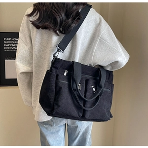 Detailed back view of a black corduroy shoulder bag showing multi-pocket design on a model