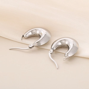 Macro shot of silver chunky U-shape hollow hoop earrings on beige silk fabric