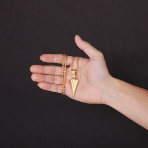 Detailed close-up of a gold-tone arrow pendant necklace worn for men's hip hop streetwear