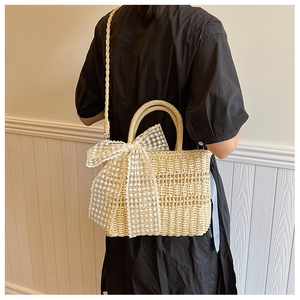 Detail of straw woven crossbody bag featuring a large white lace bow and top handle