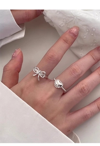 Detail of silver S925 heart and bow rings worn together on hand for a delicate aesthetic