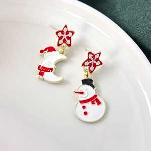 Detailed view of asymmetric Christmas earrings with snowman and moon on a ceramic plate