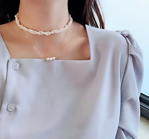 Detailed view of layered 14K gold pearl necklace on model with lavender top