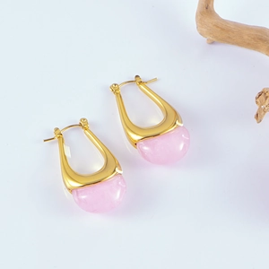 Détail de boucles d'oreilles dorées en U avec résine rose sur une surface blanche nette