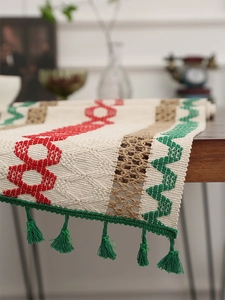 Close-up of a rustic woven table runner with red and green embroidery and green tassels