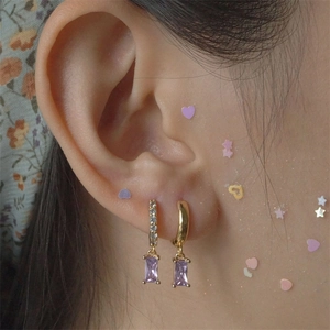 Macro shot of gold hoop earrings with purple rectangular zircon pendant on ear