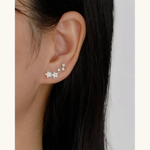 Macro shot of silver S925 star stud earrings with clear diamonds on model's ear