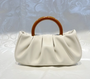 Detail of white pleated leather handbag with round amber resin handle on fabric