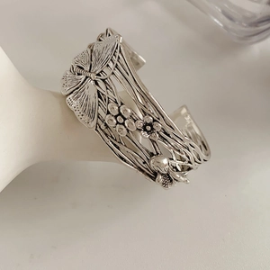 Detail of vintage silver cuff bracelet featuring intricate butterfly and floral relief