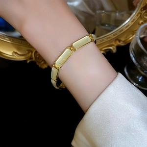 Close-up of gold plated geometric bracelet with cat eye stone on a wrist with silk