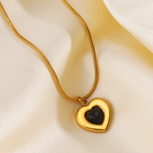Golden heart pendant necklace with black gemstone inlay on soft cream satin fabric