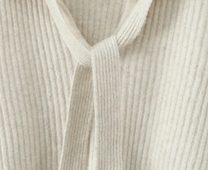 Detailaufnahme des Schnürkragen-Designs eines weichen, cremefarbenen Stricksets