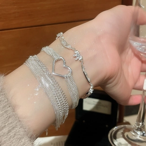 Detail of layered silver heart and floral bracelets worn on a sparkling wrist
