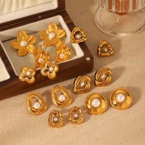 Detail of assorted gold pearl earrings featuring floral and geometric designs on wood