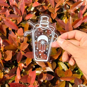 Detail of a crescent moon and star bottle prism sticker held against autumn leaves