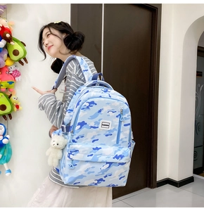 Side view of blue camouflage school backpack with bear pendant on a young model