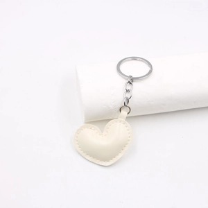 Close-up of cream white heart-shaped PU leather keychain with metal ring on white stand