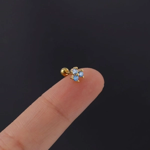 Close-up of a tiny gold screw-back stud earring with three blue zircon stones on a finger