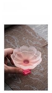 Detail of hand holding a pink lotus glass tea cup with translucent petal texture