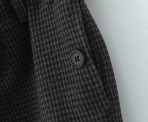 Detail shot of the dark grey houndstooth wool fabric and black button of the skirt