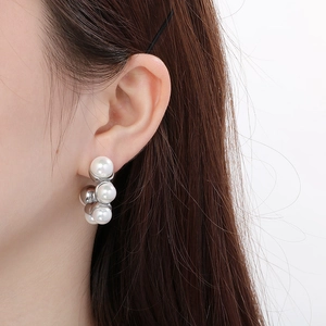 Détail de boucles d'oreilles en acier argenté en forme de C avec perles blanches