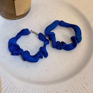 Close-up of Klein blue pleated fabric hoop earrings on a white ceramic tray with a candle
