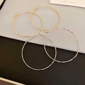 Detail of large gold and silver hoop earrings with hammered texture on minimalist background