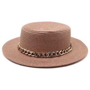 Detailed close-up of brown flat top straw hat with textured weave and gold chain detail