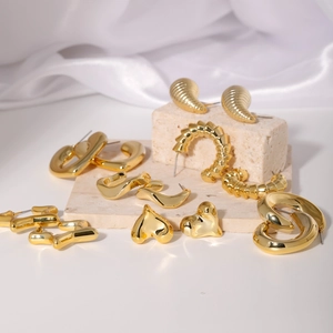 Elegant gold geometric earrings set with heart and shell designs on white silk
