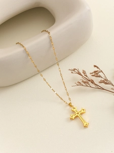Detail of a vintage golden cross pendant with relief patterns on white ceramic base