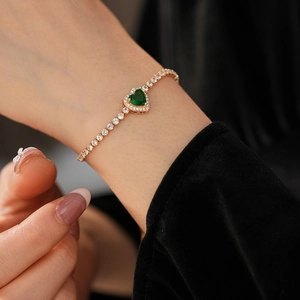 Close-up of heart-shaped emerald bracelet with cubic zirconia set on a gold-plated tennis chain