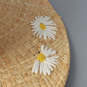 Handwoven raffia straw sun hat featuring white daisy accents and detailed weaving texture