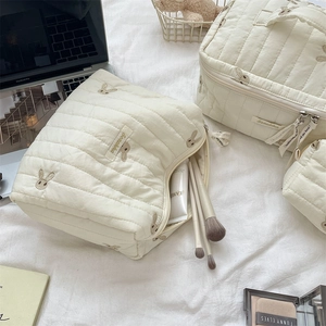Close-up of quilted cream makeup bags featuring delicate rabbit embroidery and soft fabric
